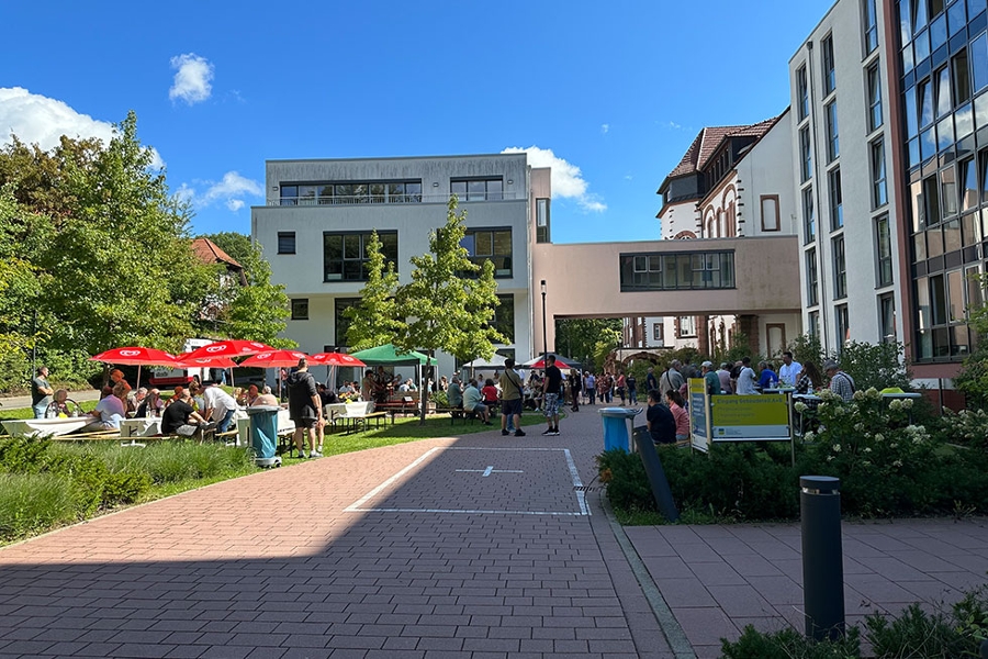 Die Gäst des Ehemaligentreffens sitzen auf Bierbänken vor dem Klinikgebäude zusammen und unterhalten sich. Die Gäst des Ehemaligentreffens sitzen auf Bierbänken vor dem Klinikgebäude zusammen und unterhalten sich.