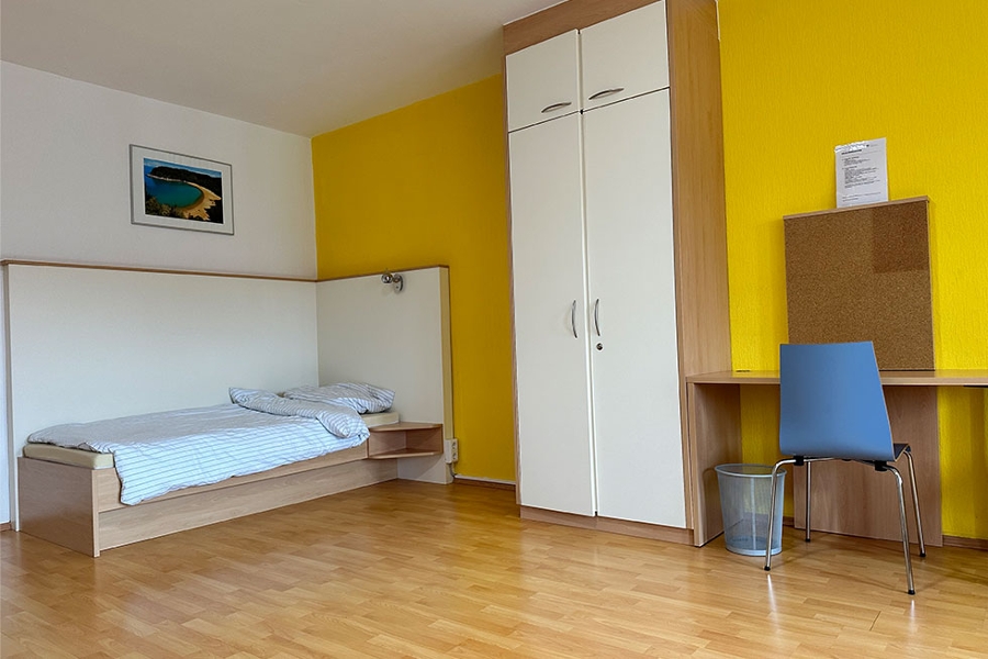 Ein Einzelbett, links daneben ein Schrank und ein Schreibtisch Ein Einzelbett, links daneben ein Schrank und ein Schreibtisch